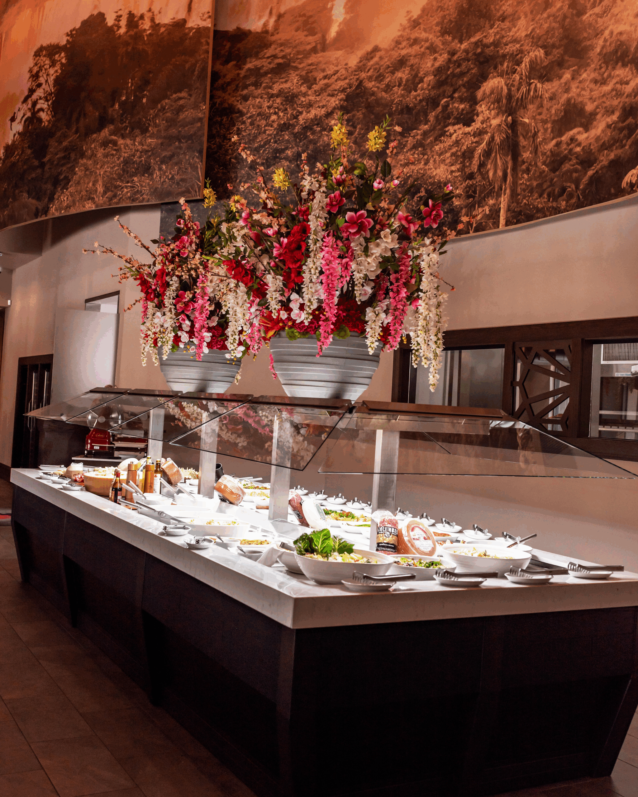 Salad bar at Chama Gaucha Dallas featuring fresh greens, charcuterie, and house made specialties displayed under floral arrangements.