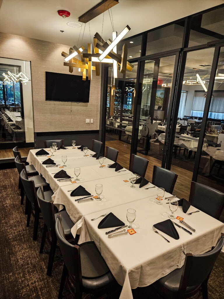 Houston private dining room with long banquet table, glass wall, and elegant event setup at Chama Gaucha